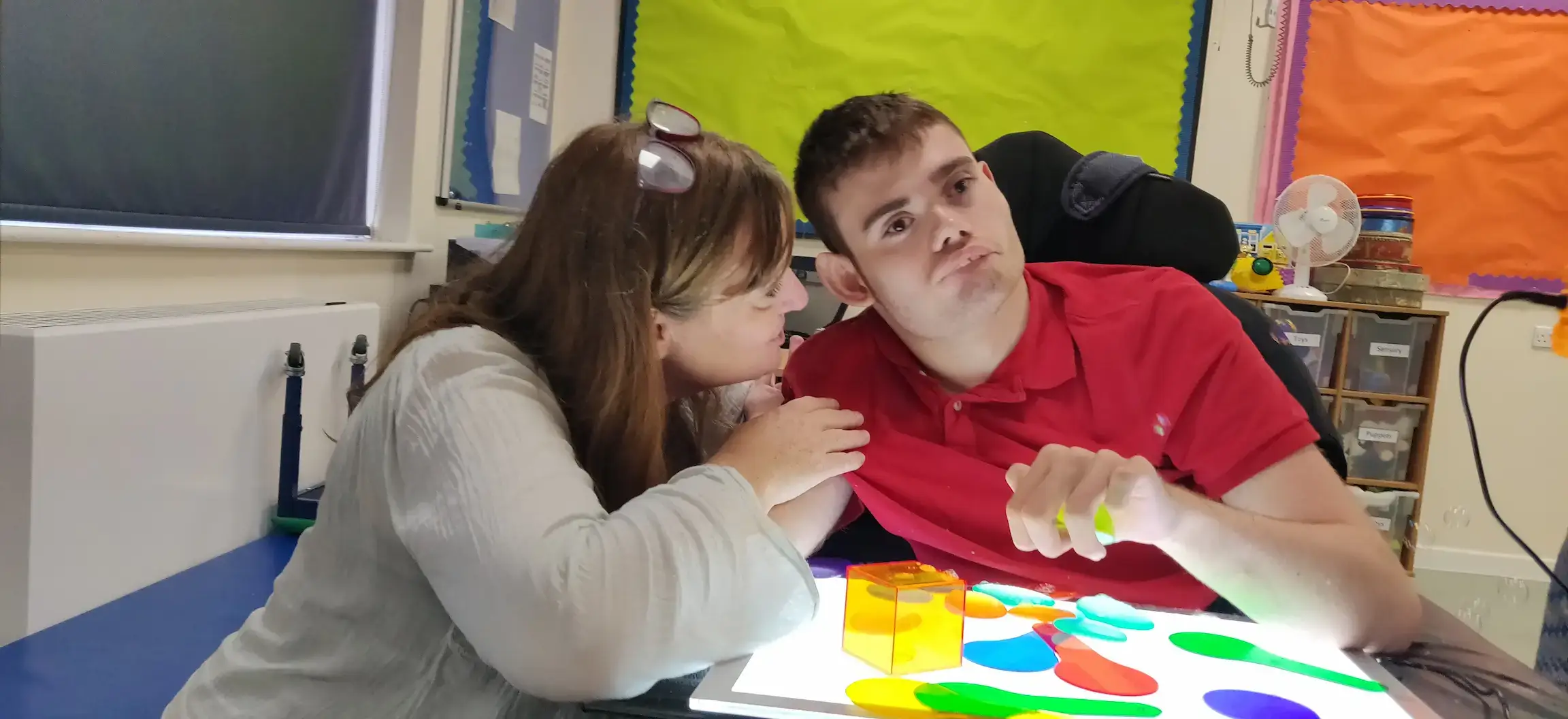 2) A support worker actively listening to someone in a safe, sensory-friendly space